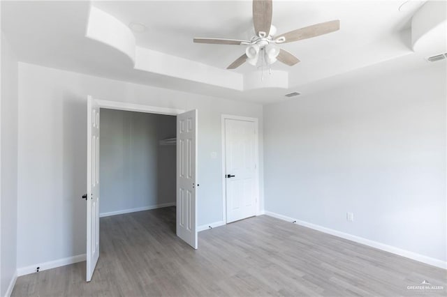 unfurnished bedroom with light wood-type flooring, a closet, a raised ceiling, and ceiling fan