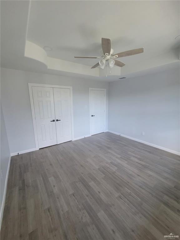 unfurnished bedroom with ceiling fan, dark hardwood / wood-style floors, a raised ceiling, and a closet