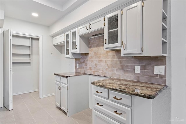 kitchen featuring decorative backsplash, light tile patterned floors, white cabinets, and dark stone counters