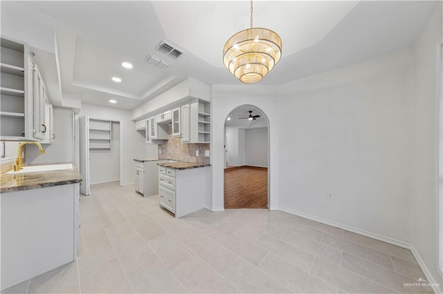 kitchen featuring tasteful backsplash, sink, white cabinets, and a tray ceiling