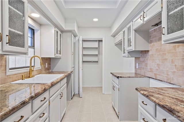 kitchen with light tile patterned flooring, tasteful backsplash, sink, white cabinets, and light stone countertops