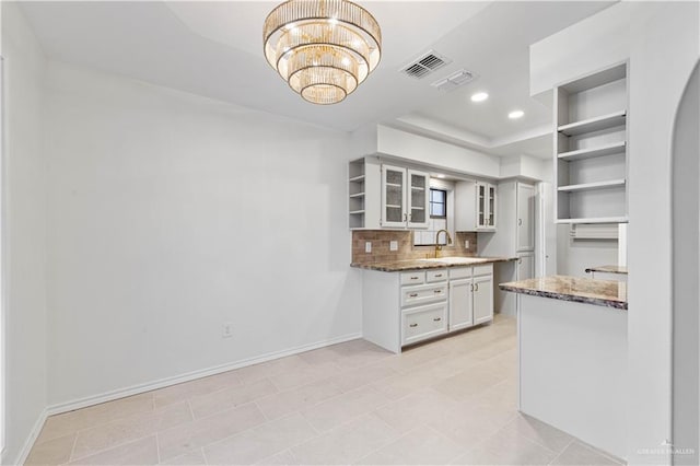 kitchen with an inviting chandelier, dark stone counters, sink, and backsplash