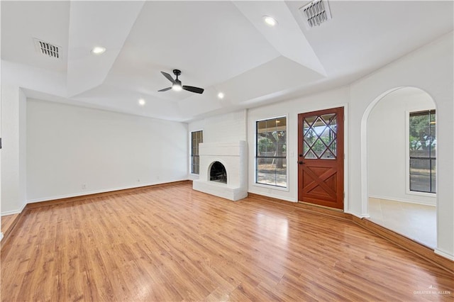 unfurnished living room with ceiling fan, a fireplace, a tray ceiling, and light hardwood / wood-style floors