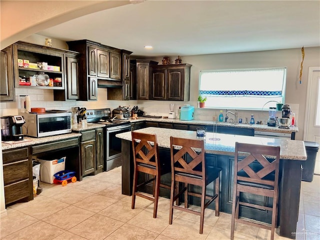 kitchen featuring dark brown cabinetry, a center island, light stone counters, a breakfast bar, and appliances with stainless steel finishes