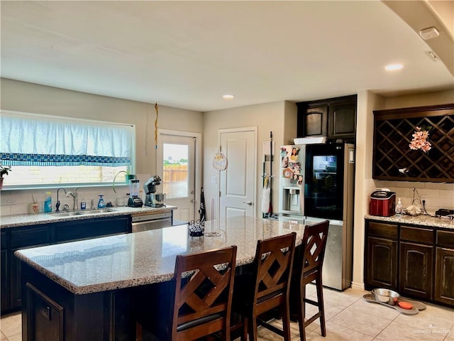 kitchen with dark brown cabinets, a center island, light stone counters, and sink