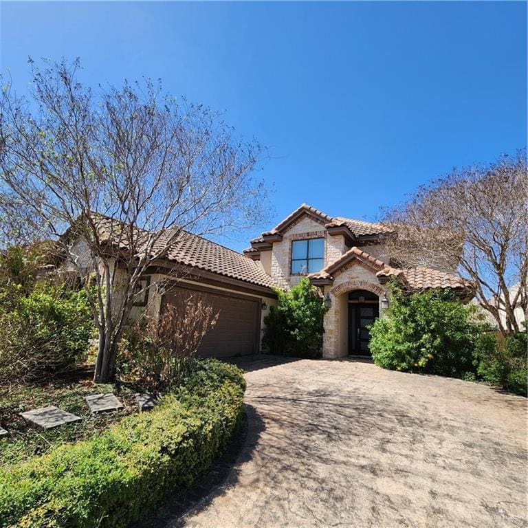 view of front of property with driveway, an attached garage, stucco siding, stone siding, and a tile roof