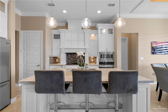 kitchen with pendant lighting, white cabinetry, stainless steel appliances, light stone countertops, and an island with sink