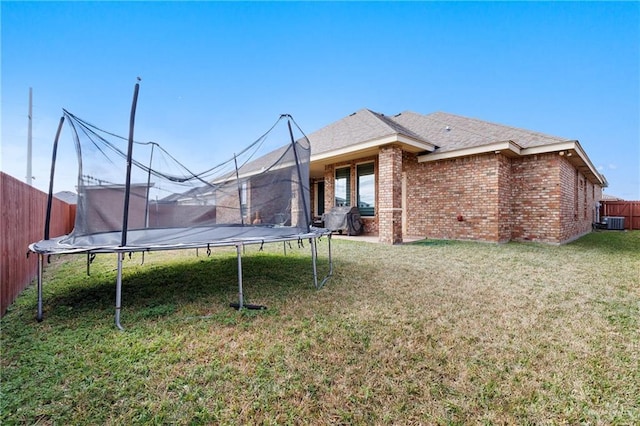 rear view of house featuring a trampoline, central AC, and a lawn