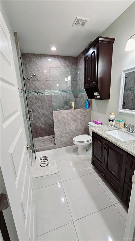 bathroom featuring tile patterned floors, vanity, toilet, and a tile shower