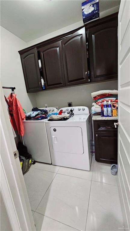 clothes washing area featuring separate washer and dryer, light tile patterned floors, and cabinets