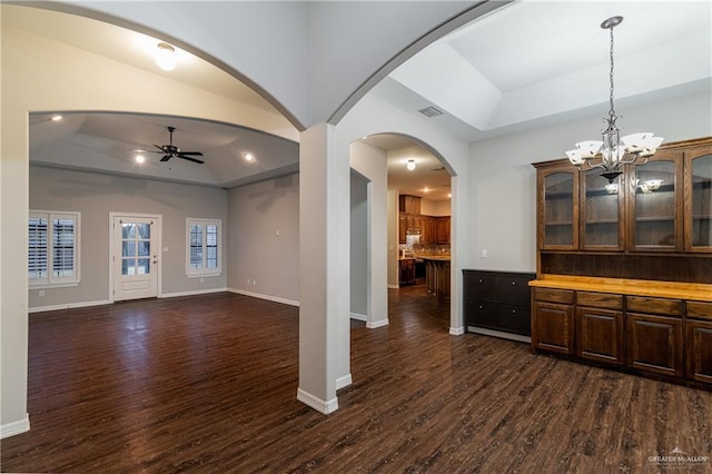 interior space with pendant lighting, ceiling fan with notable chandelier, a raised ceiling, and dark wood-type flooring