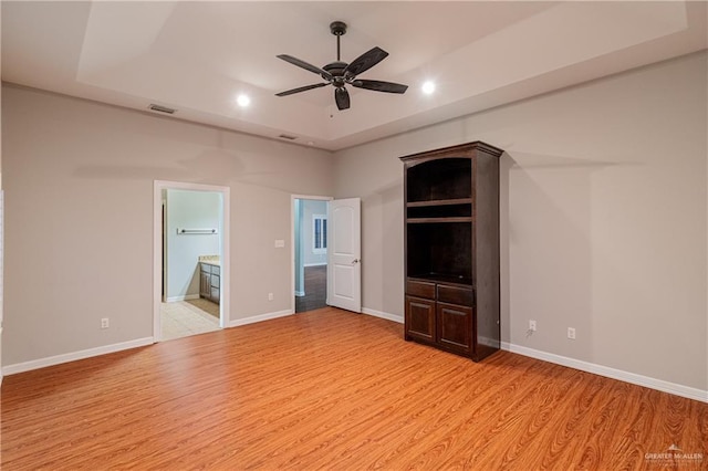 unfurnished bedroom with ensuite bathroom, ceiling fan, a raised ceiling, and light wood-type flooring