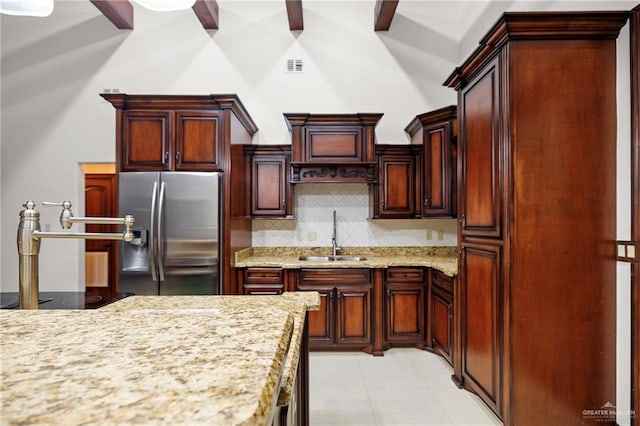 kitchen with tasteful backsplash, sink, stainless steel fridge, light stone countertops, and beam ceiling