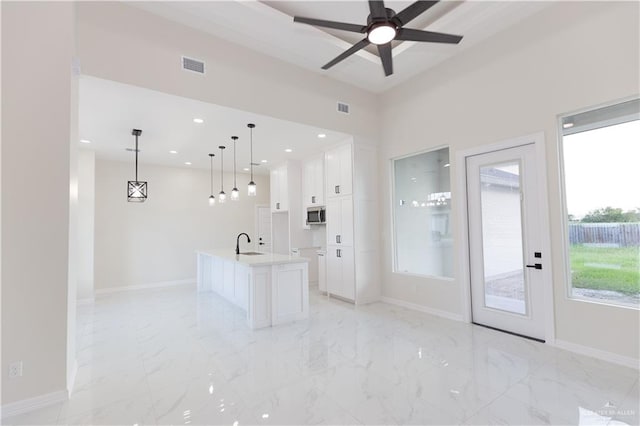 kitchen with white cabinetry, sink, ceiling fan, decorative light fixtures, and a kitchen island with sink