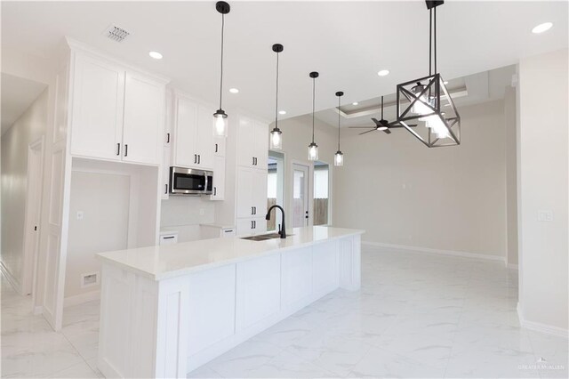 kitchen with a center island with sink, white cabinets, decorative light fixtures, and sink