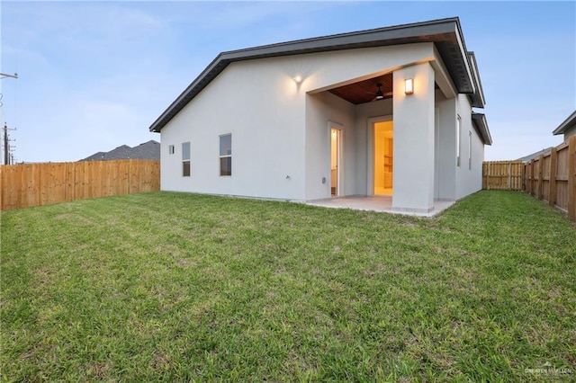 back of house featuring ceiling fan, a fenced backyard, a yard, a patio area, and stucco siding