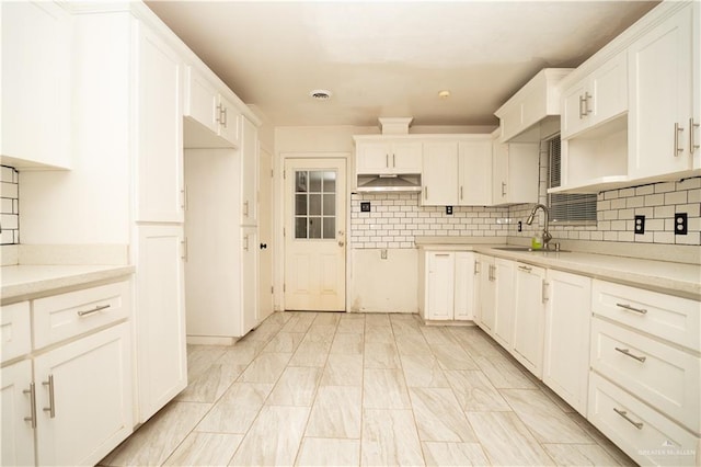 kitchen featuring decorative backsplash, white cabinets, light stone countertops, and sink