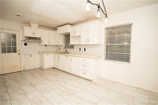 kitchen featuring backsplash, ornamental molding, sink, pendant lighting, and white cabinetry