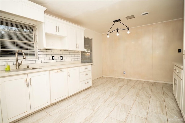 kitchen featuring decorative backsplash, sink, white cabinets, and hanging light fixtures