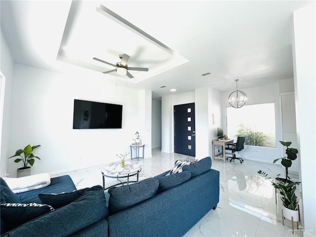 living room featuring ceiling fan with notable chandelier and a raised ceiling