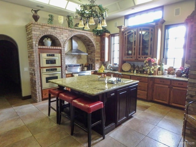 11213 N Fm 88th Blvd, Weslaco, TX 78599 - kitchen featuring backsplash, arched walkways, an island with sink, wall chimney range hood, and appliances with stainless steel finishes