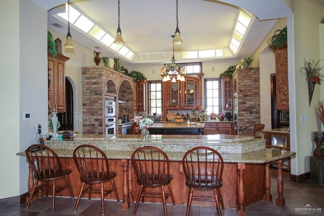 11213 N Fm 88th Blvd, Weslaco, TX 78599 - kitchen with arched walkways, glass insert cabinets, decorative light fixtures, and light stone counters
