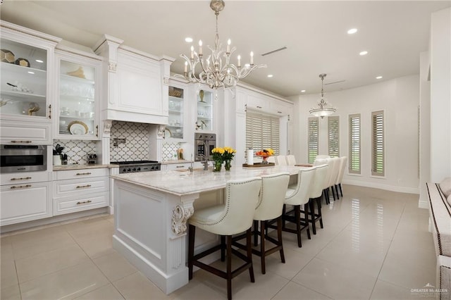 kitchen with pendant lighting, white cabinetry, tasteful backsplash, light stone countertops, and a center island with sink