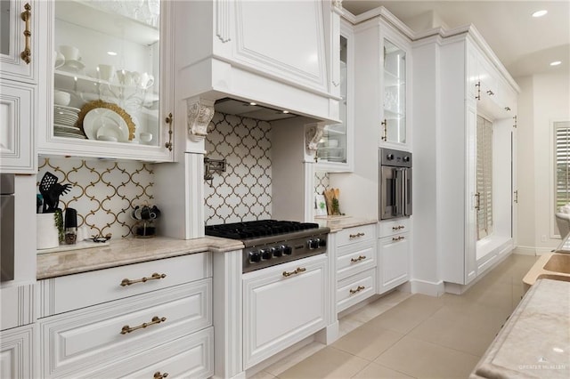 kitchen featuring light tile patterned floors, appliances with stainless steel finishes, white cabinetry, tasteful backsplash, and custom range hood