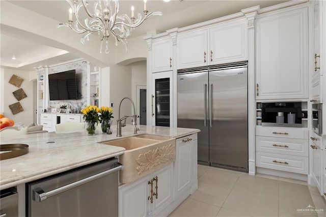 kitchen with light tile patterned floors, stainless steel appliances, light stone countertops, white cabinets, and decorative light fixtures