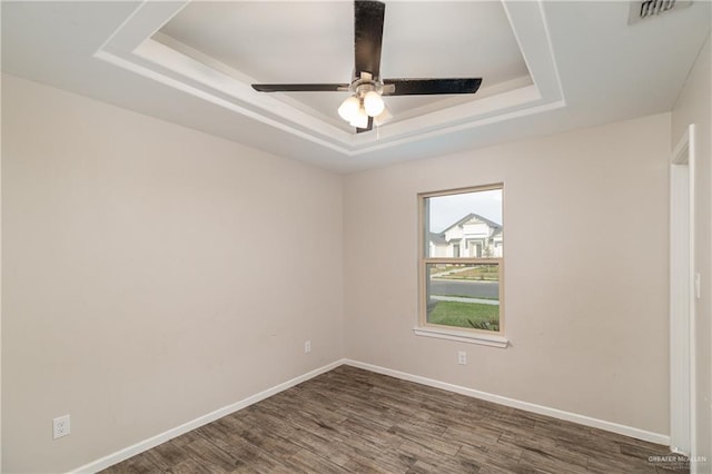 empty room with wood finished floors, a raised ceiling, visible vents, and baseboards