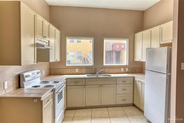 kitchen with light tile patterned floors, white appliances, tile countertops, and sink