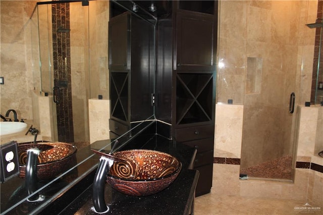 bathroom with sink, a shower with door, and tile walls