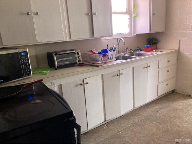 kitchen featuring black range, white cabinetry, and sink