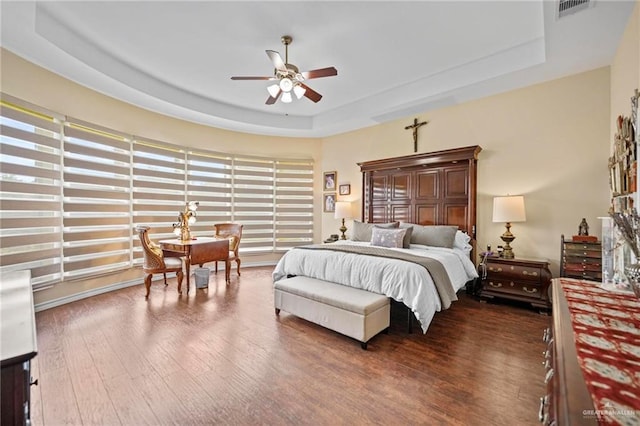 bedroom with dark hardwood / wood-style floors, ceiling fan, and a raised ceiling