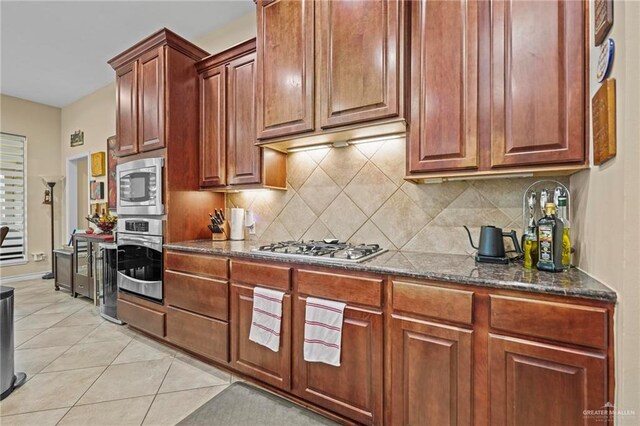 kitchen with decorative backsplash, light tile patterned floors, stainless steel appliances, and dark stone counters