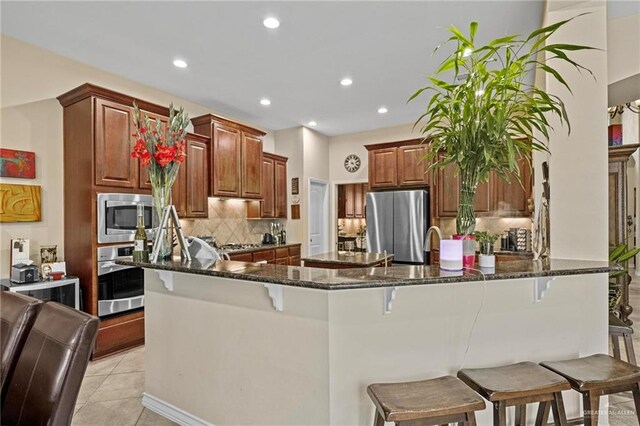 kitchen with a kitchen bar, kitchen peninsula, stainless steel appliances, light tile patterned floors, and dark stone countertops