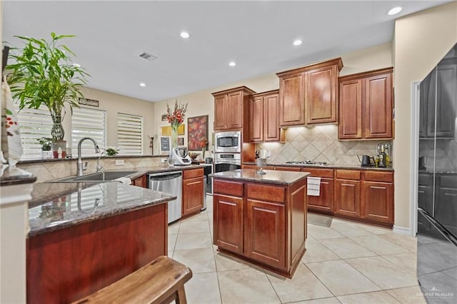 kitchen with appliances with stainless steel finishes, sink, dark stone countertops, a center island, and light tile patterned flooring