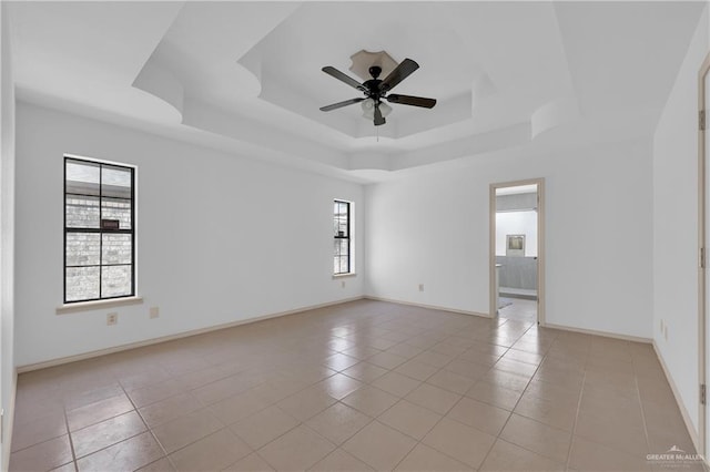 spare room with ceiling fan, a tray ceiling, light tile patterned flooring, and baseboards