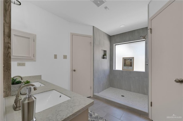 full bath featuring double vanity, visible vents, a sink, tiled shower, and tile patterned floors