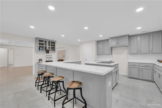 kitchen with gray cabinets, a kitchen island, glass insert cabinets, and light countertops