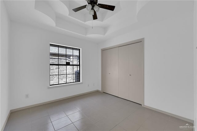 unfurnished bedroom with a closet, a raised ceiling, light tile patterned flooring, ceiling fan, and baseboards