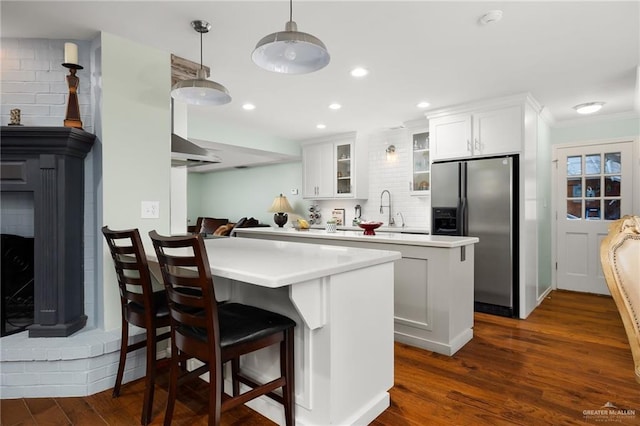 kitchen featuring dark wood-type flooring, light countertops, stainless steel refrigerator with ice dispenser, decorative backsplash, and glass insert cabinets