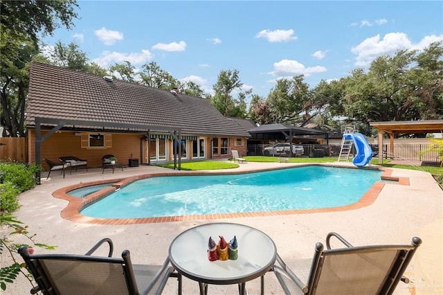 view of swimming pool with a patio, a water slide, fence, and a pool with connected hot tub