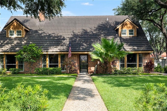 view of front of house with a tiled roof, a front yard, a chimney, and brick siding