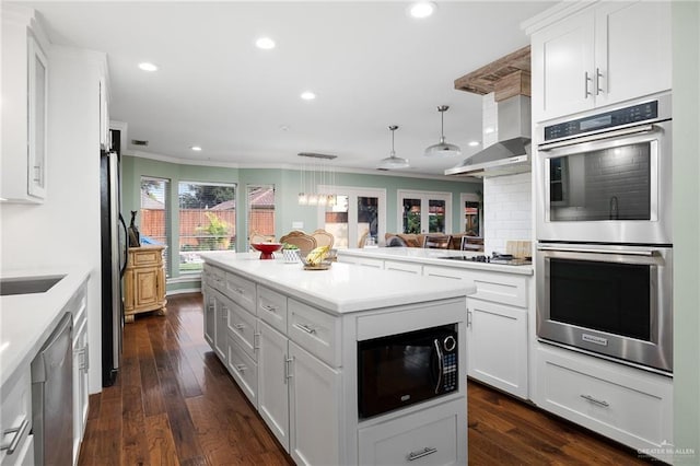 kitchen featuring white cabinets, appliances with stainless steel finishes, decorative backsplash, wall chimney exhaust hood, and crown molding