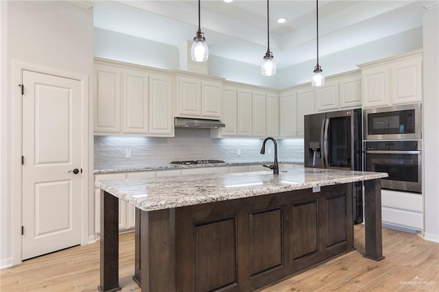 kitchen with pendant lighting, appliances with stainless steel finishes, tasteful backsplash, light stone countertops, and light wood-style flooring