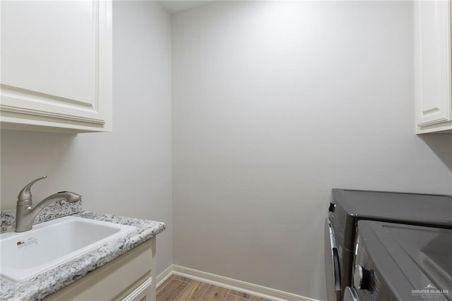 washroom featuring washer and dryer, baseboards, light wood-style flooring, a sink, and cabinet space