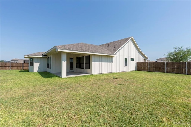 back of house with board and batten siding, roof with shingles, a lawn, a fenced backyard, and a patio