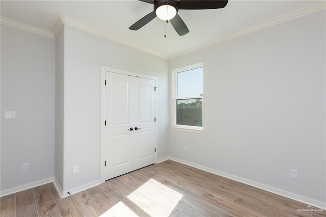 unfurnished bedroom featuring crown molding, light wood-style flooring, a ceiling fan, baseboards, and a closet