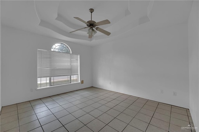 tiled empty room with a raised ceiling and ceiling fan